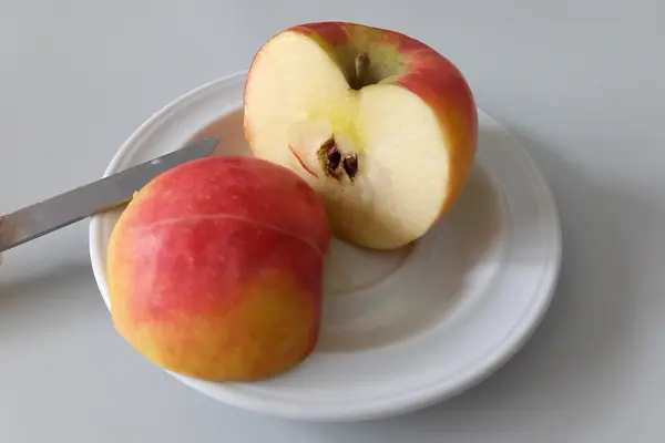 In Hälften geschnittener roter Apfel auf weißem Teller
