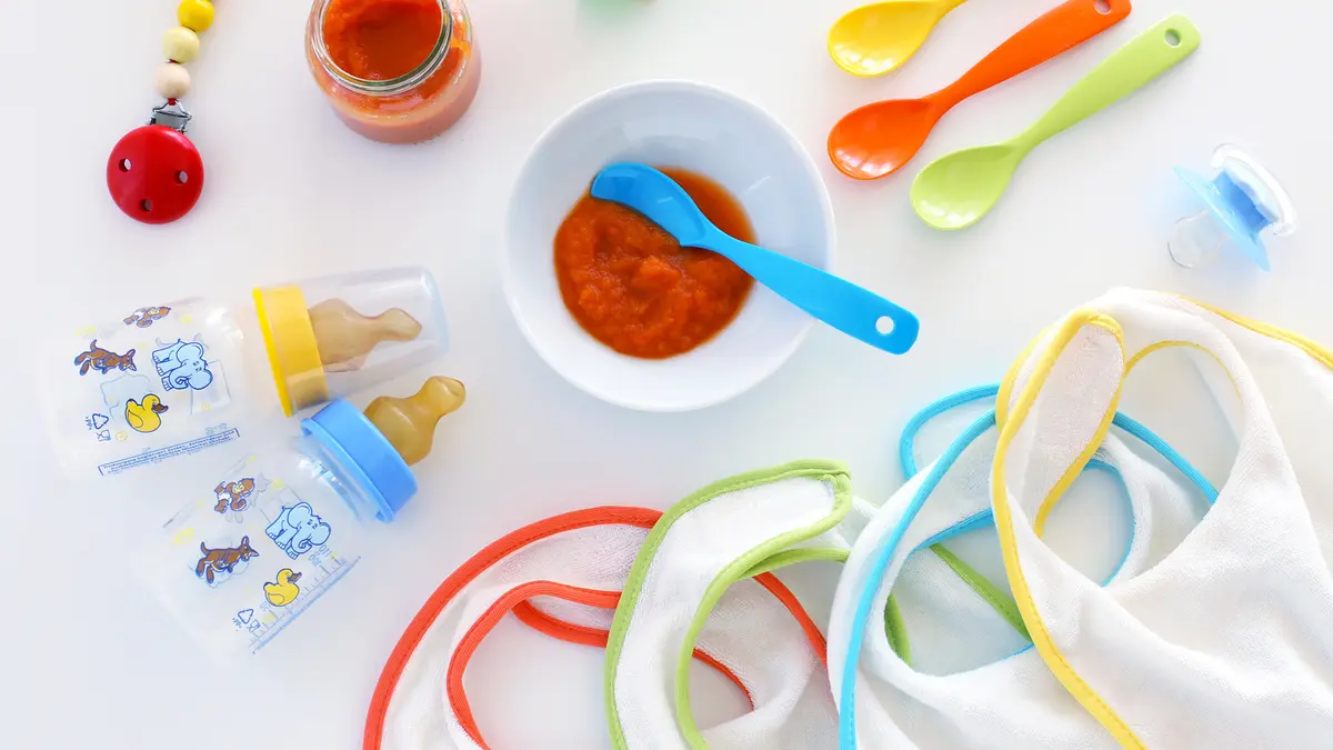 Babyutensielen, wie Schnuller und Plastikbesteck, liegen auf einem Tisch