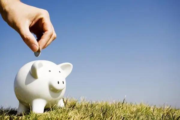 Hand wirft Geld in ein Sparschwein