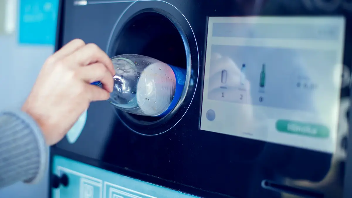 Hand legt Flasche in Pfandautomat