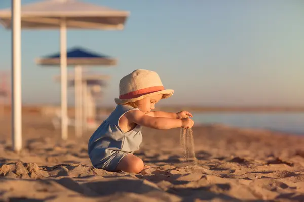 Ein Kind spielt am Strand im Sand und trägt einen Hut gegen die Sonne