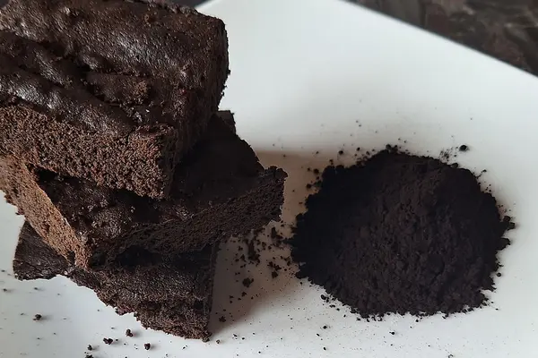 Ein Schokokuchen liegt auf einem Teller, daneben ein Häufchen mit schwarzem Kakaopulver