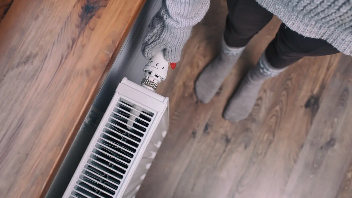 Frau mit Handschuh dreht an Thermostat der Heizung