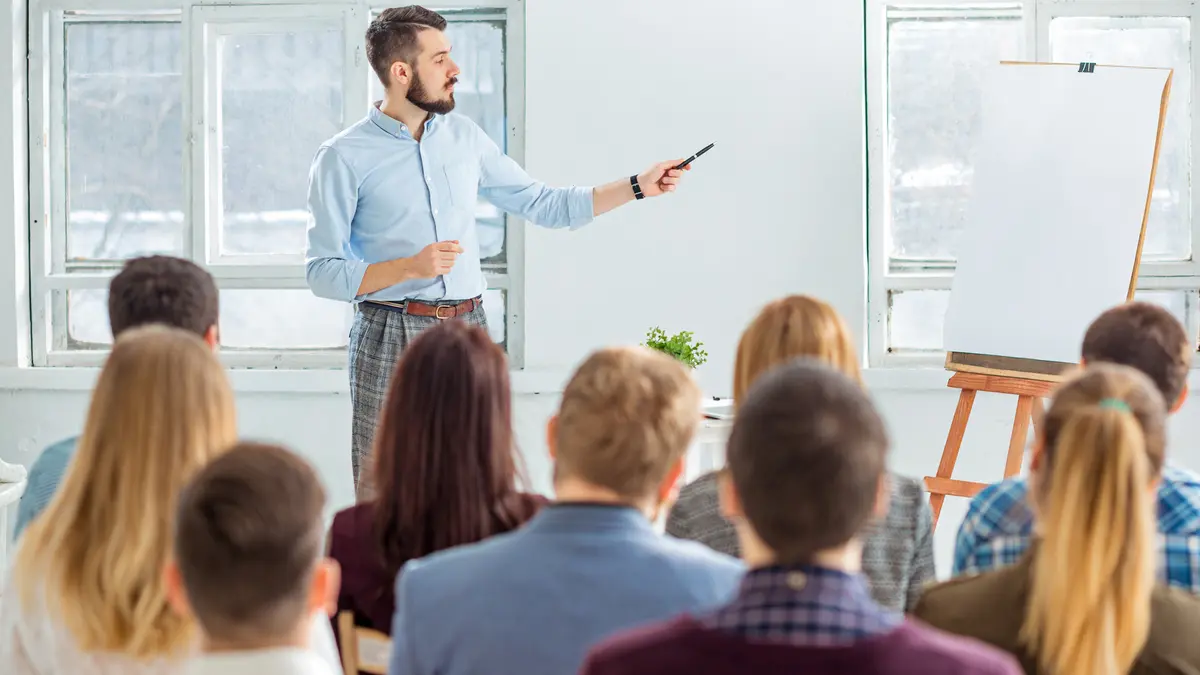 Ein Redner steht vor Publikum und erklärt etwas mit Hilfe eines Flipcharts.