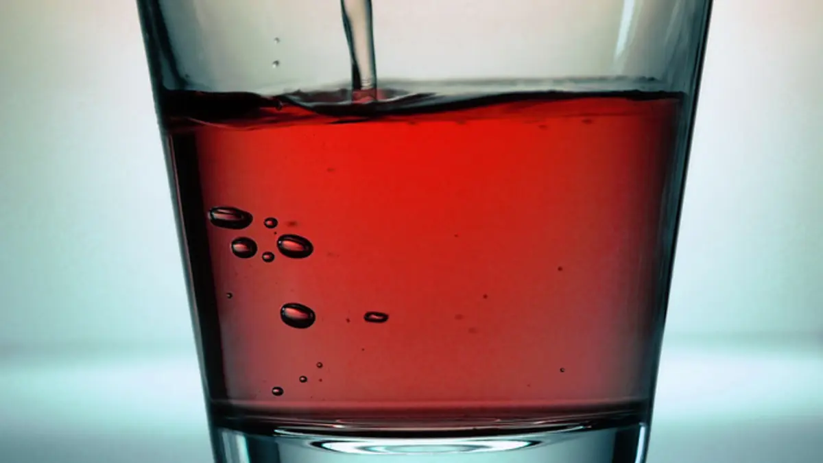Ein Glas mit roter Flüssigkeit wird mit weiterer Flüssigkeit gefüllt. Saftschorle