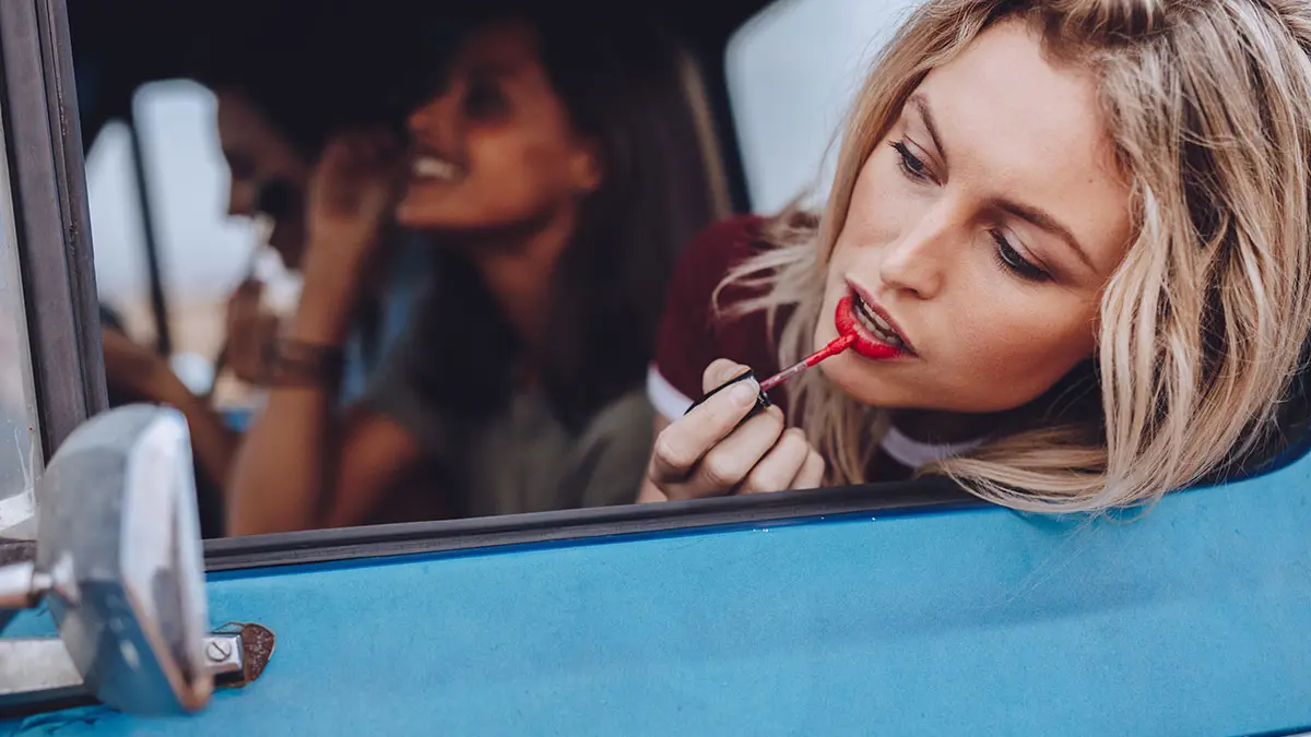 Zwei Frauen in einem blauen Auto, eine malt sich die Lippen an