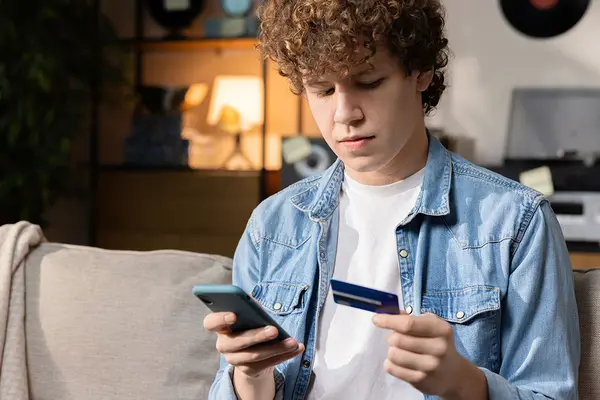 Teenager beim Online-Shopping mit Smartphone und Kreditkarte auf dem Sofa