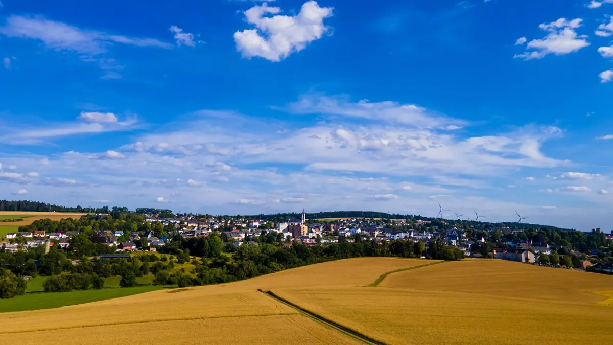 Ein weites Feld mit einem Ort im Hintergrund und blauem Himmel.