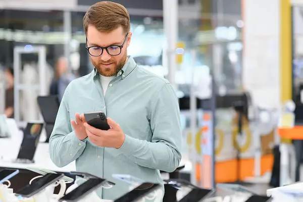 Mann sucht Smartphone in Elektronikmarkt aus