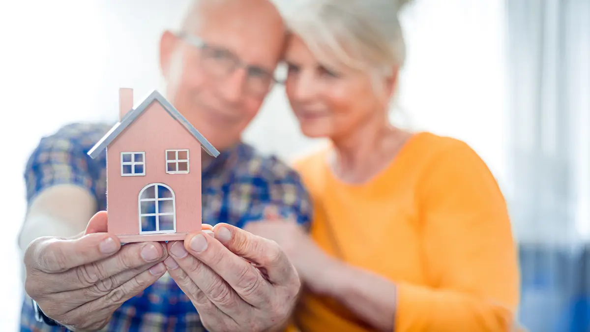 Älteres Ehepaar halten ein kleines Haus in den Händen