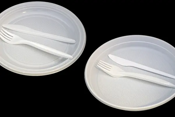 Zwei weiße Plastikteller, Plastikgabeln und Plastikmesser nebeneinander