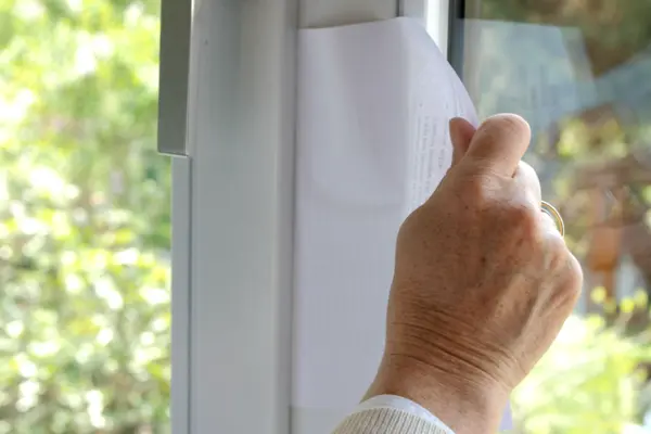 Hand zieht an Papier im Fensterrahmen