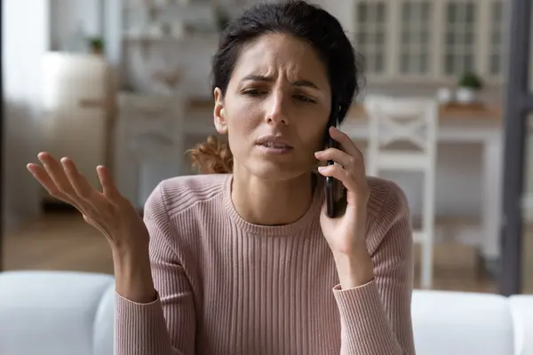 junge Frau mit dunklem Haar telefoniert mit verärgertem Gesicht
