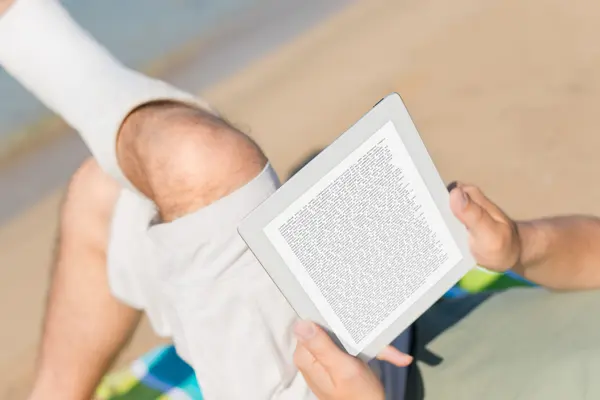 Jemand liegt mit einem Bein im Gips am Strand und liest ein Buch.