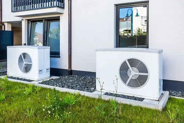 Zwei Wärmepumpen stehen vor der Hauswand eines Mahrfamilienhauses