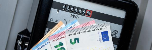 Ein Stromzähler, vor den jemand mehrere Geldscheine hält.