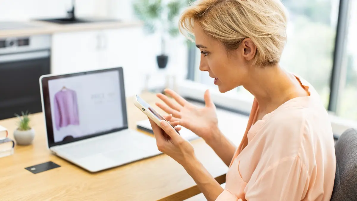 Eine Frau sitzt vor ihrem Laptop und telefoniert mit dem Kundenservice eines Onlineshops.