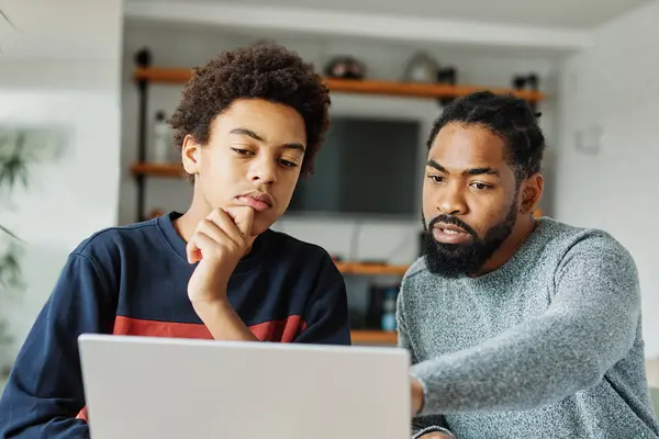 Ein Vater und sein Sohn sitzen vor dem Laptop und grübeln.