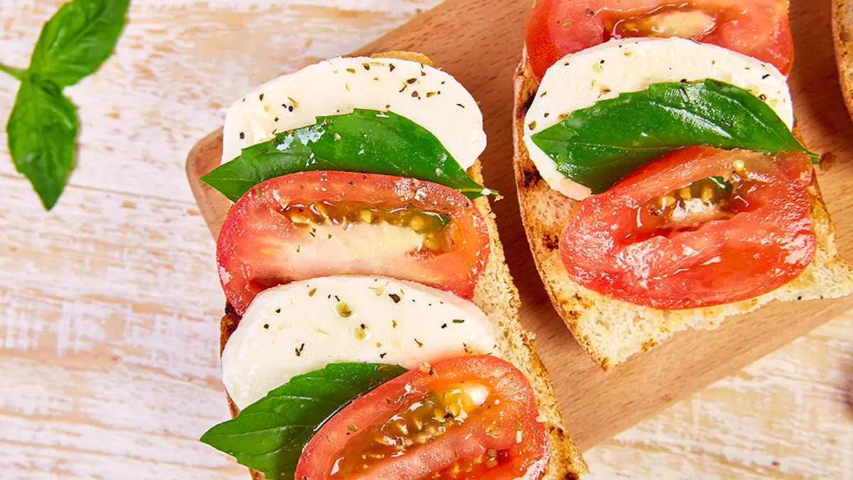 Bruschetta mit Tomate, Mozzarella und Basilikum auf einem Brettchen