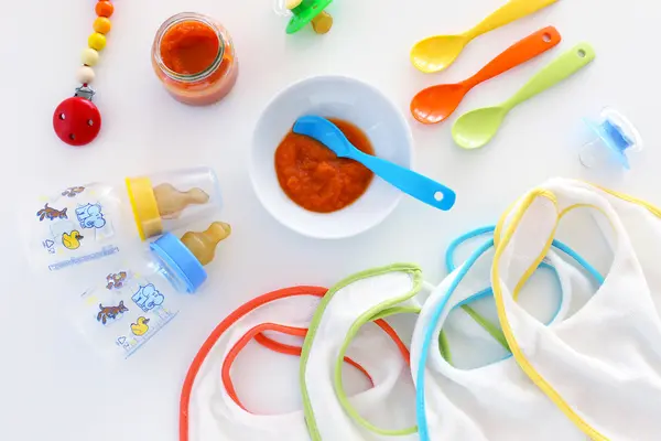 Babyutensielen, wie Schnuller und Plastikbesteck, liegen auf einem Tisch