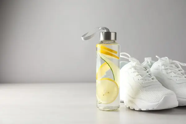 Eine Trinkflasche, die mit Wasser und Zitronenscheiben gefüllt ist, steht neben einem Paar weißer Turnschuhe.