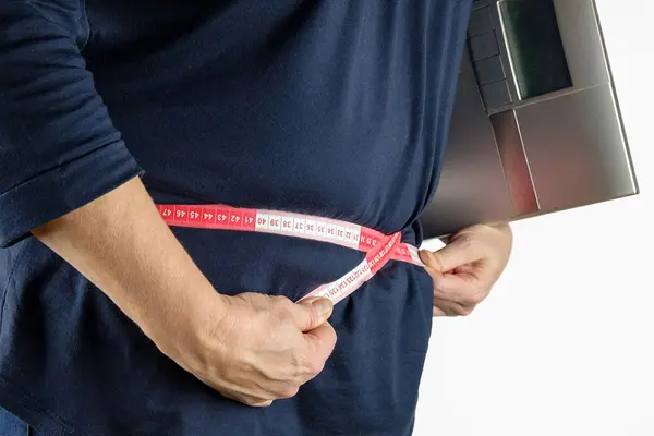 Eine Person misst mit dem Bandmaß ihren Bauchumfang, sie hat eine Waage unter ihren Arm geklemmt