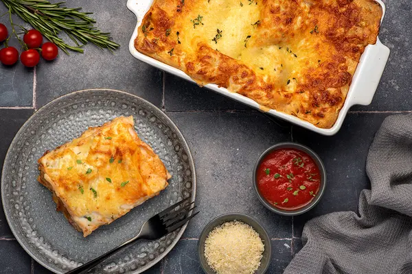Lasagne in einer Auflaufform, ein Stück auf einem Teller.