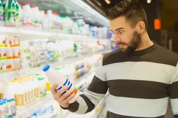 Mann mit überraschtem Gesichtsausdruck liest Verpackungstext im Supermarkt