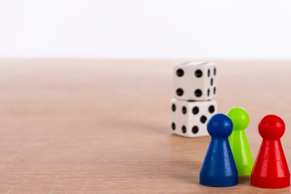 drei Spielfiguren (blau, grün, rot) am rechten Bildrand, im Hintergrund zwei Würfel