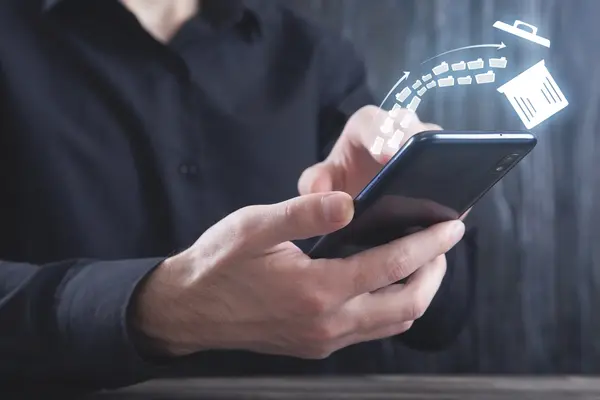 Ein Mann in einem schwarzen Hemd hält ein Smartphone in den Händen. Über dem Display schwebt eine digitale Illustration, die zeigt, wie mehrere Aktenordner-Symbole in einen Papierkorb fliegen, was den Vorgang des Löschens oder Aufräumens von Daten symbolisiert.