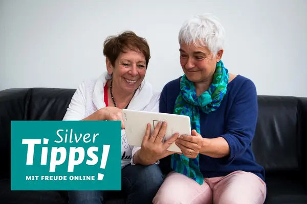 Zwei ältere Frauen auf einem Sofa schauen auf ein Tablet.