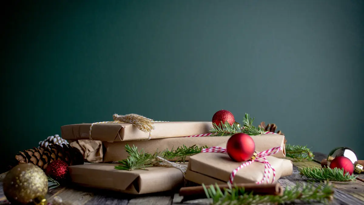 Weihnachtsgeschenke, die in Packpapier verpackt sind sowie Weihnachtskugeln und Tannen
