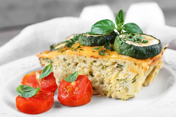 Ein Stück Gemüsetarte auf einem Teller, garniert mit Zucchini, Tomate und Basilikum