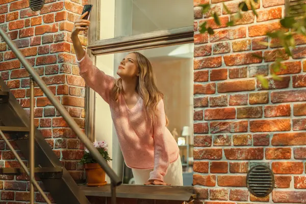 Frau lehnt sich aus dem Fenster und hält Handy nach oben.