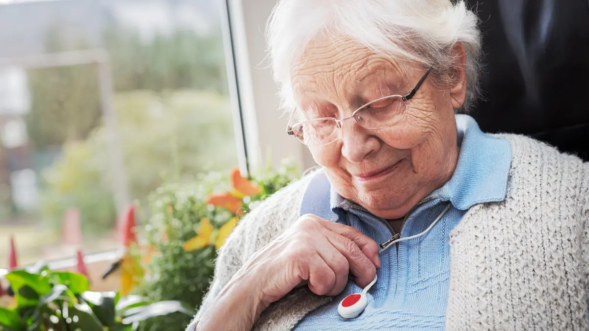 Seniorin trägt Hausnotruf-Knopf als Kette um den Hals