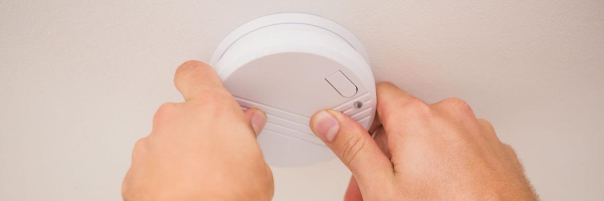 Zwei Hände arbeiten an einem Rauchmelder an der Decke