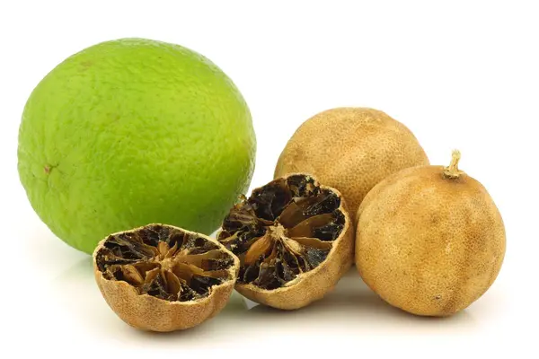 Eine aufgeschnittene schwarze Zitrone liegt neben zwei ganzen schwarzen Zitronen und einer Limette.