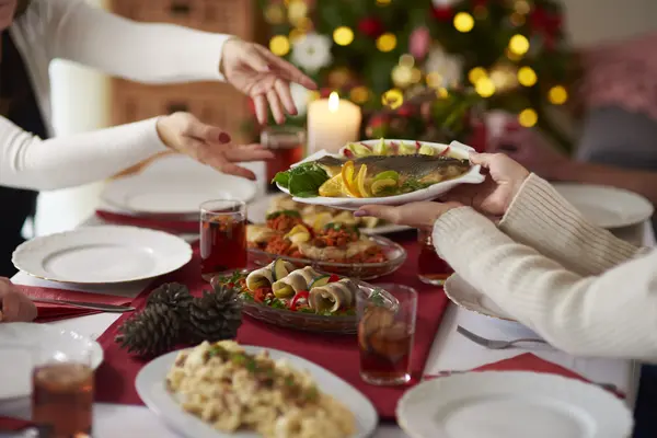 Menschen, die Teller mit Weihnachtskarpfen über festlich gedecktem Tisch passieren, im Hintergrund sieht man einen geschmückten Weihnachtsbaum