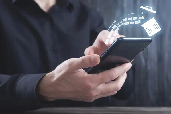 Ein Mann in einem schwarzen Hemd hält ein Smartphone in den Händen. Über dem Display schwebt eine digitale Illustration, die zeigt, wie mehrere Aktenordner-Symbole in einen Papierkorb fliegen, was den Vorgang des Löschens oder Aufräumens von Daten symbolisiert.