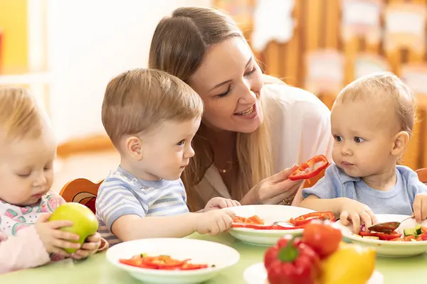 Eine Frau sitzt mit drei Kleinkindern beim Essen am Tisch