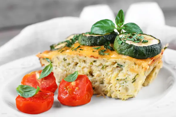 Ein Stück Gemüsetarte auf einem Teller, garniert mit Zucchini, Tomate und Basilikum