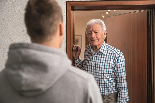 Älterer Mann öffnet seine Wohnungstür. Davor steht ein junger Mann.