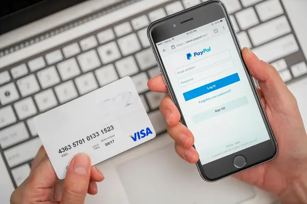 Auf einem Handy wird der Paypal-Login Screen angezeigt. Daneben sieht man eine Kreditkarte