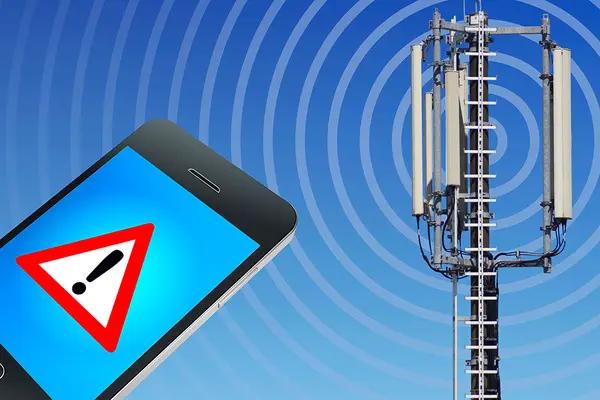 Smartphone mit Achtung-Symbol auf dem Display neben Mobilfunkmast