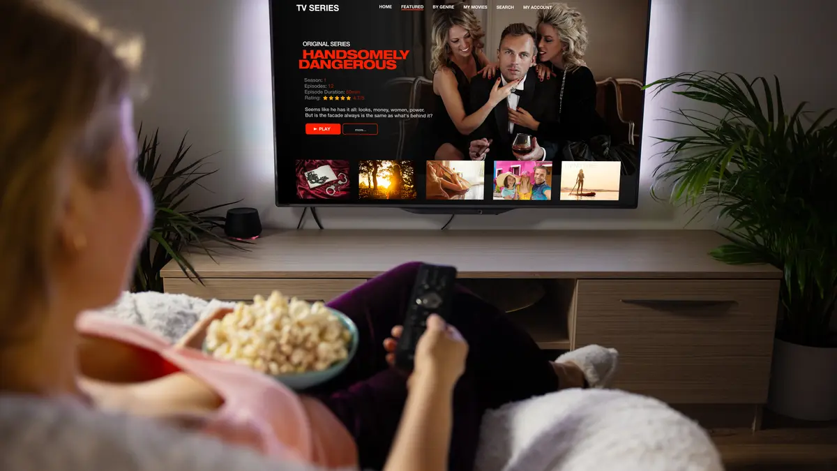 Frau schaut Serie über Streaming-Dienste mit Popocorn zuhause.