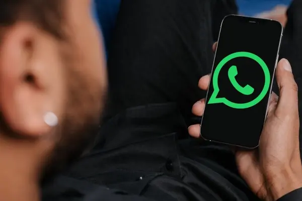 Mann mit Smartphone in der Hand, auf dessen Display das grüne Logo von WhatsApp zu sehen ist.