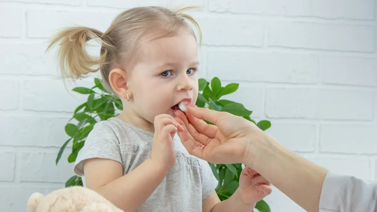Erwachsene Person, die einem kleinen Mädchen beine Vitamintablette gibt