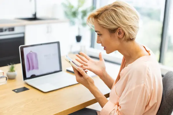 Eine Frau sitzt vor ihrem Laptop und telefoniert mit dem Kundenservice eines Onlineshops.