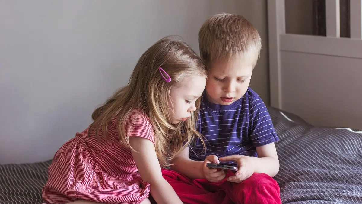 Zwei kleine Kinder sitzen auf dem Sofa und schauen in ein Smartphone.