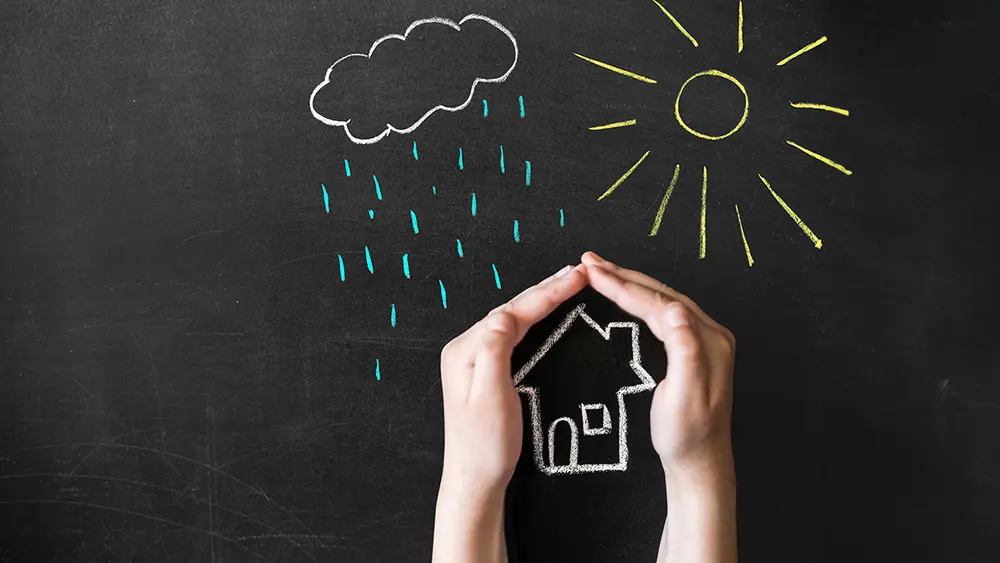 Hand schützt gezeichnetes Haus vor gezeichneten Regen- und Sonnenstrahlen